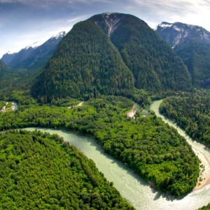 Ein Landschaftspanorama des Toba Valleys mit Bergmassiven im Hinter- und den waldigen Ufern des Flusses im Vordergrund.